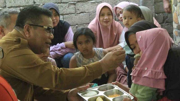 Kepala Dinas Pemberdayaan Perempuan Perlindungan Anak dan Keluarga Berencana Lotim, H. Ahmat menyuapi salah satu anak pada acara peluncuran MBG. (ekbisntb.com/rus)