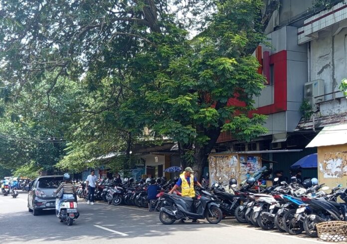 PARKIR - Seorang juru parkir mengatur kendaraan di pinggir Jalan Cilinaya yang dipotret beberapa waktu lalu. Pemkot Mataram pangkas target retribusi parkir menjadi Rp12 miliar. (Ekbis NTB/pan) Pemkot Mataram Pangkas Target Retribusi Parkir 2026 Menjadi Rp12 Miliar